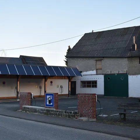 Carport mit Solarmodulen auf dem Dach und mehreren Wallboxen an einer Ladestation in Mörsdorf (Hunsrück), dahinter ein Hausdach mit PV-Anlage
